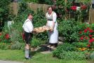 zwei Menschen in bayerischer Tracht halten tragen ein großes Holzbrett mit Brot.