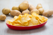 Schale mit Kartoffelchips und im Hintergrund Kartoffeln.