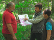 drei Menschen unterhalten sich im Wald und zeigen auf eine Karte.